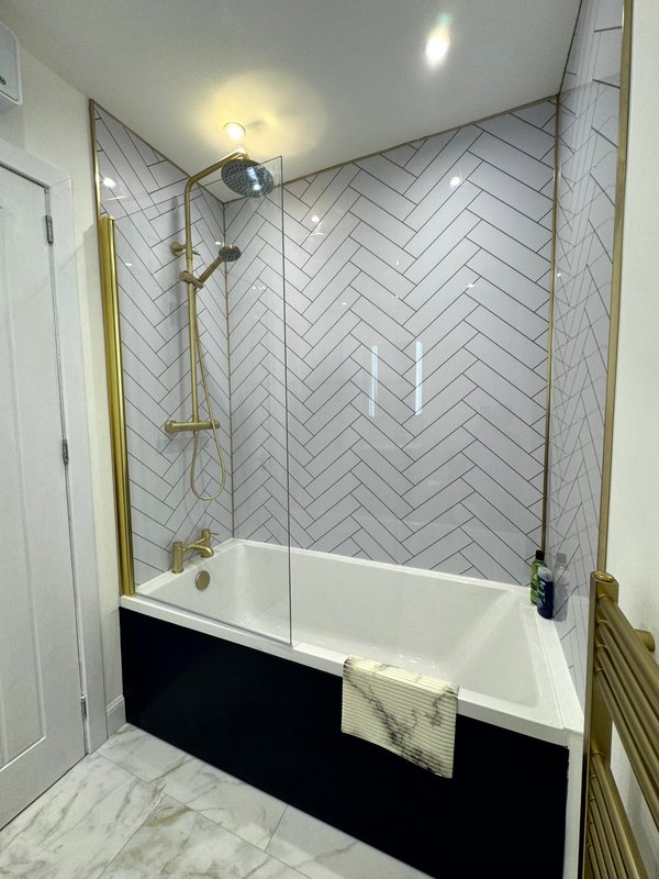 Modern bathroom with herringbone tile shower enclosure, white soaking tub, and brass fixtures