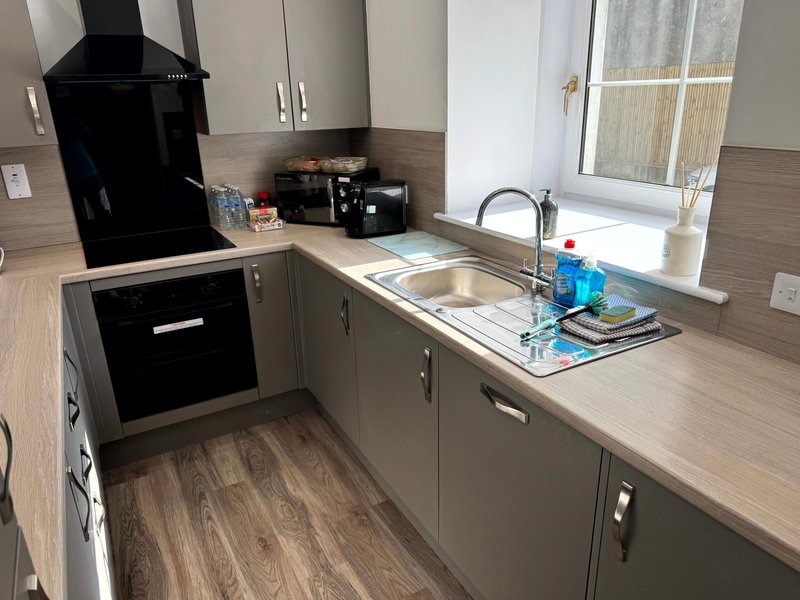 Modern kitchen with grey cabinetry, stainless steel sink, black appliances and wooden flooring