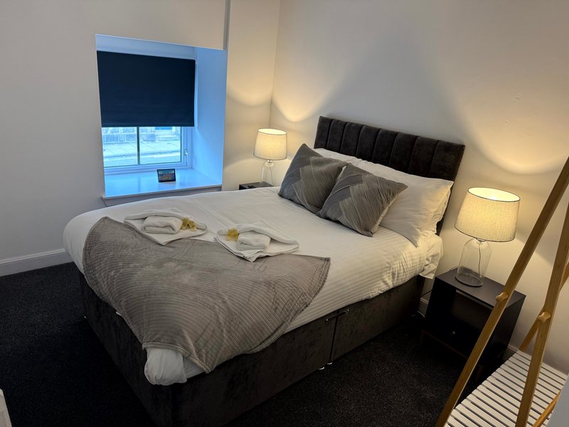 Modern bedroom with double bed, black headboard, grey bedding, and two bedside lamps