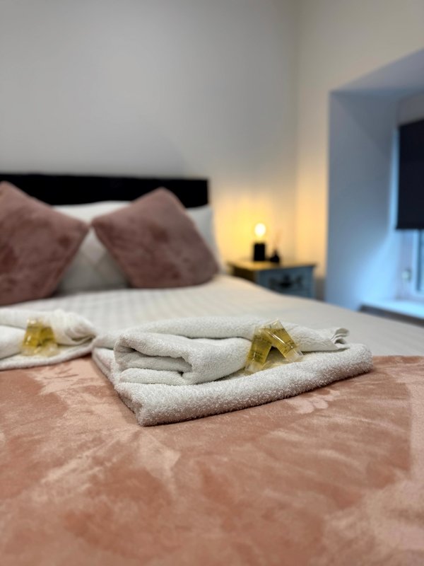 Bedroom with neatly arranged towels on bed, cushions, and bedside lamp
