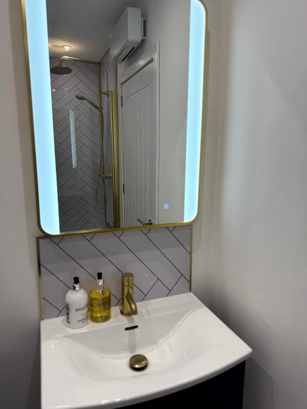 Modern bathroom with white basin, illuminated mirror, herringbone tile splashback and toiletries
