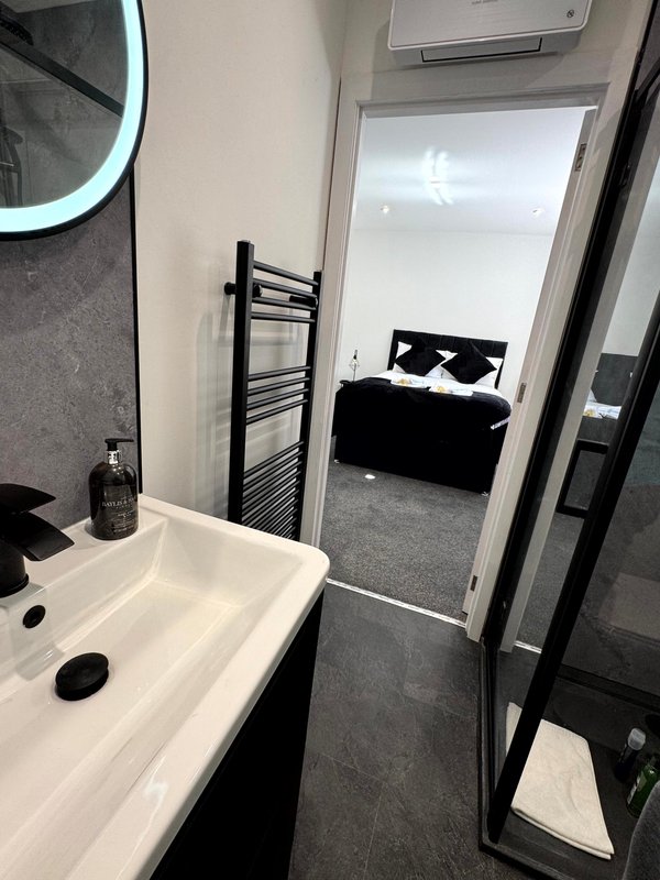 Modern bathroom with white sink, black fixtures, and view through doorway to bedroom with black bed