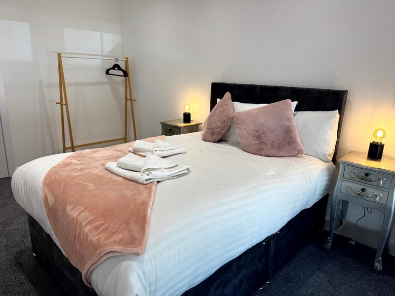 Modern bedroom with double bed, pink cushions, white bedding, and wooden clothing rack