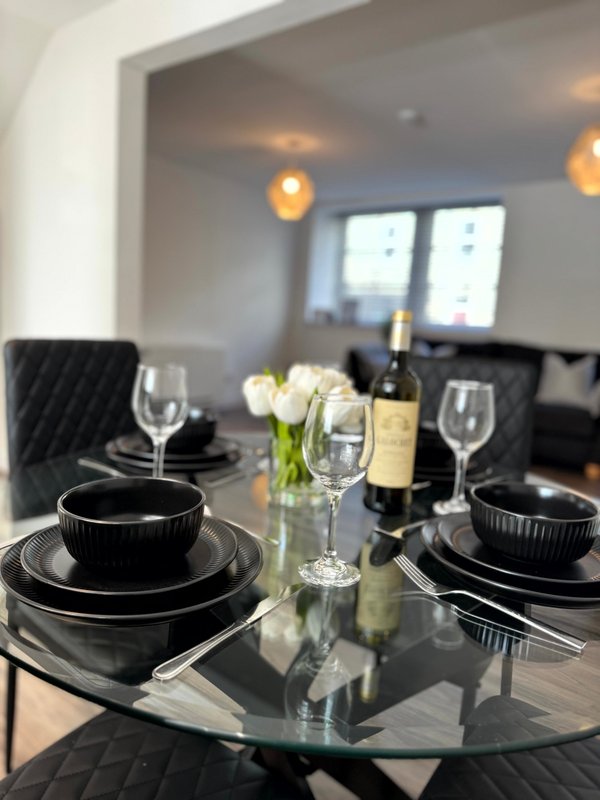 Formal dining table set with black plates, wine glasses, and bottle centerpiece