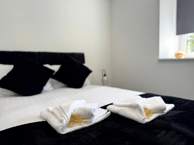 Modern bedroom with black and white bedding, folded towels, and window with blinds