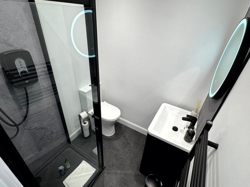 Modern bathroom with black tile walls, shower enclosure, toilet, and white sink vanity