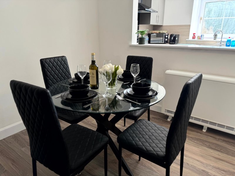 Dining area with round black table, quilted black chairs, wine bottle and white flowers