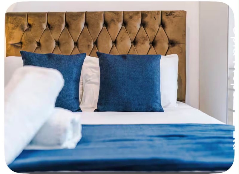 Bedroom with blue upholstered headboard, white bedding, navy cushions and throw blanket