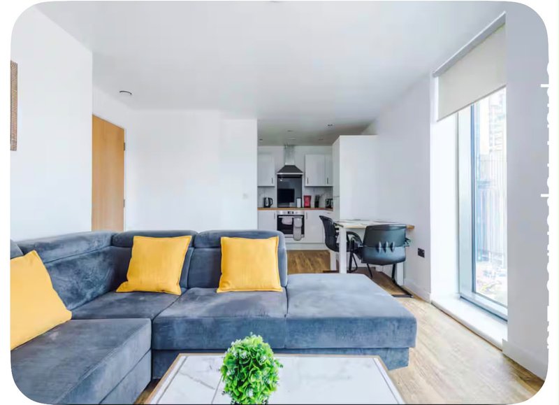 Modern living room with blue sectional sofa, yellow cushions, potted plant and open-plan kitchen area