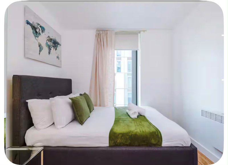 Bright modern bedroom with double bed, green throw, white pillows, and world map wall art