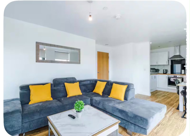 Modern open-plan living room with blue corner sofa, yellow cushions, white coffee table and kitchen visible