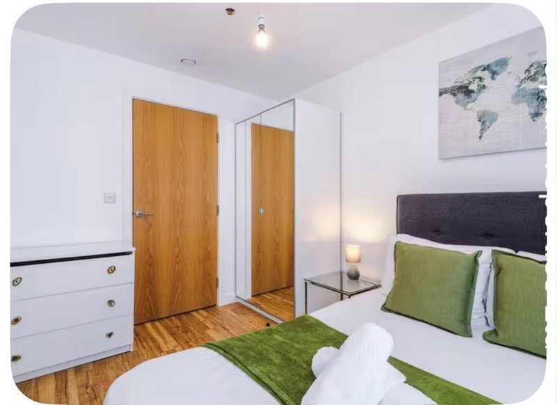 Modern bedroom with double bed, green cushions, wooden doors and white wardrobe