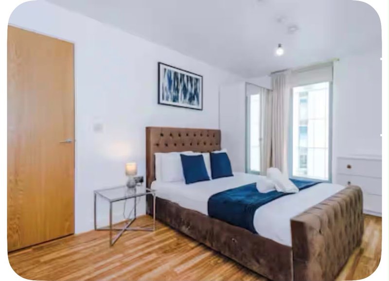 Modern bedroom with brown upholstered bed, blue cushions, wooden flooring and bright windows