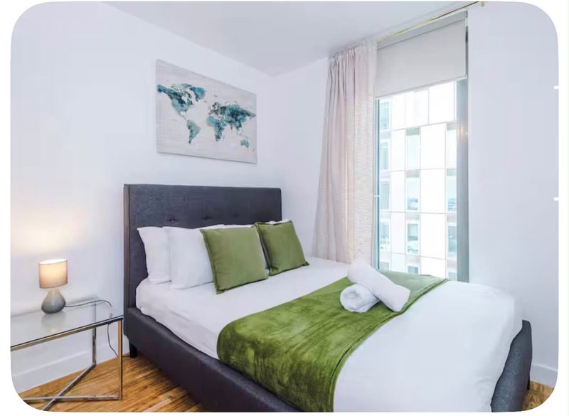 Bedroom with double bed, green bedding, dark headboard, and window with city view