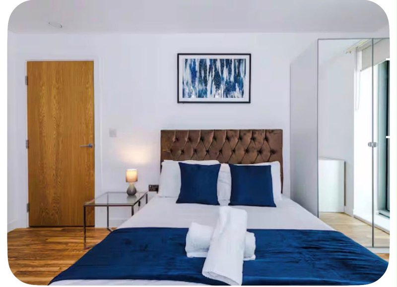 Modern bedroom with double bed, blue bedding, brown headboard, and wooden door