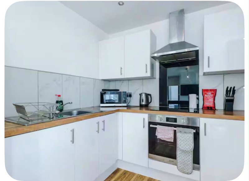 Modern kitchen with white cabinets, wooden countertop, black appliances and stainless steel extractor hood