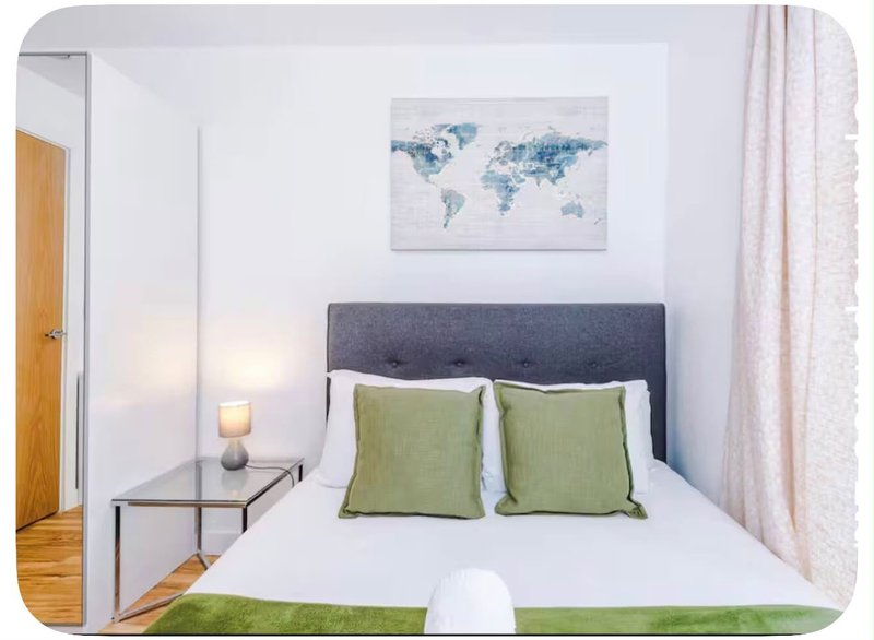 Bright bedroom with double bed, grey headboard, green cushions and world map wall art