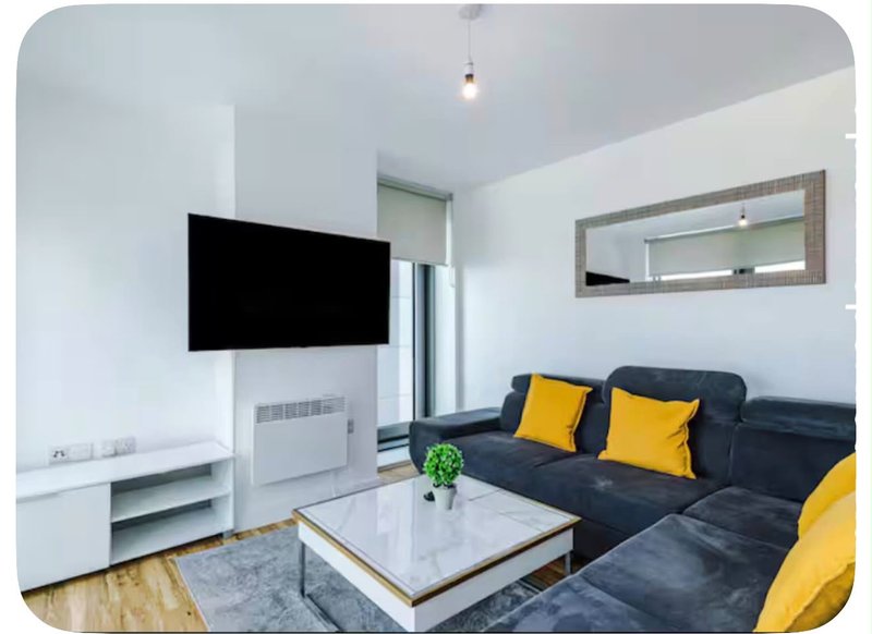 Modern living room with dark sofa, yellow cushions, wall-mounted TV, coffee table and mirror