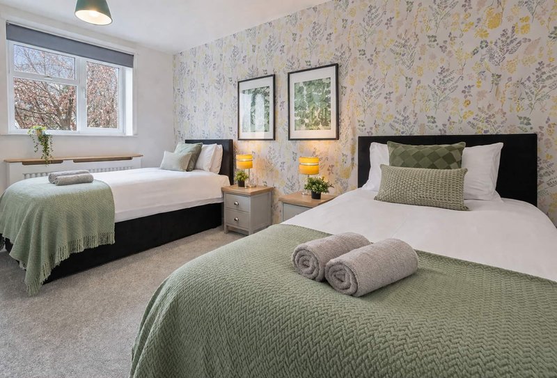 Bright twin bedroom with two beds, patterned wallpaper, framed artwork and window view