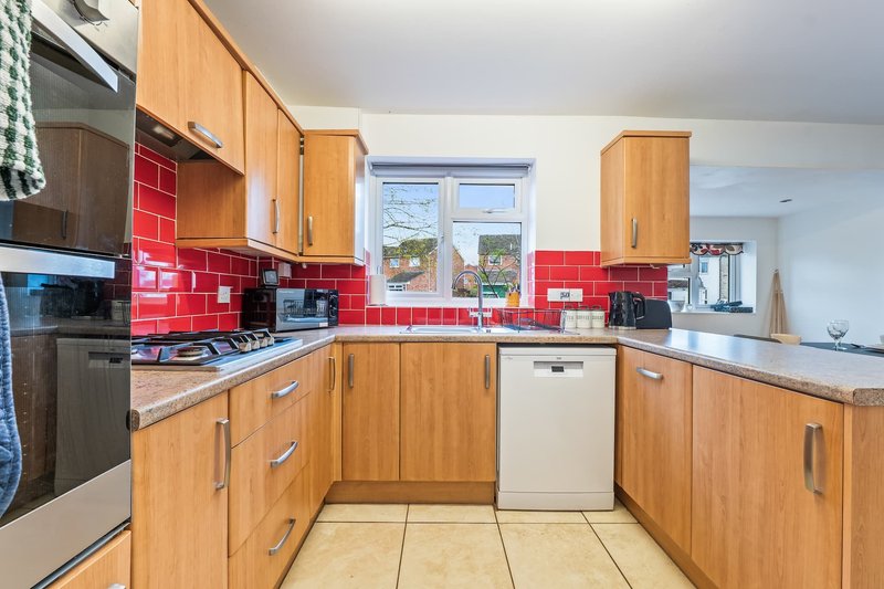 Kitchen with wooden cabinets, red tile backsplash, gas hob, and window overlooking garden