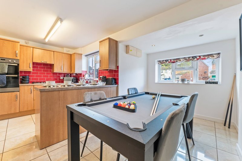 Kitchen and dining area with wooden cabinets, red tile backsplash, and pool table