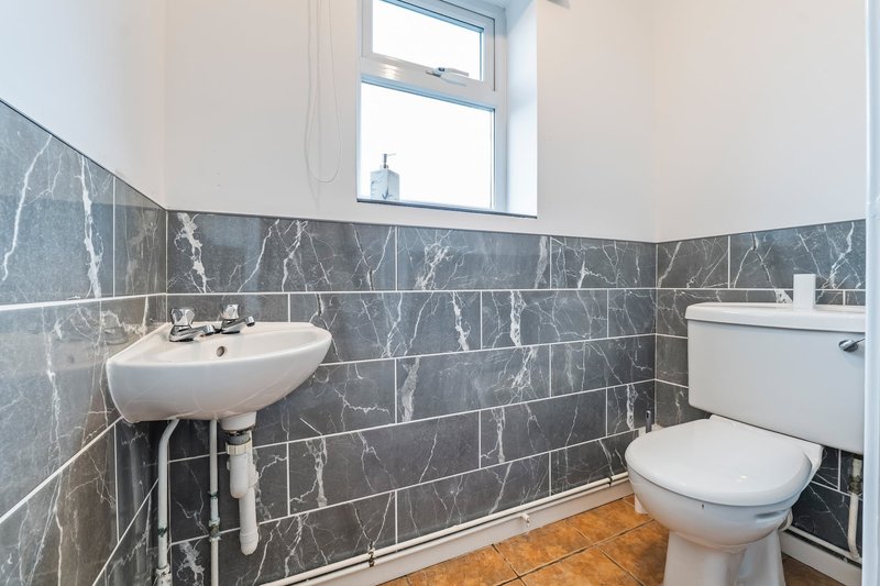 Bathroom with dark marble wall tiles, white sink, toilet, and wooden floor