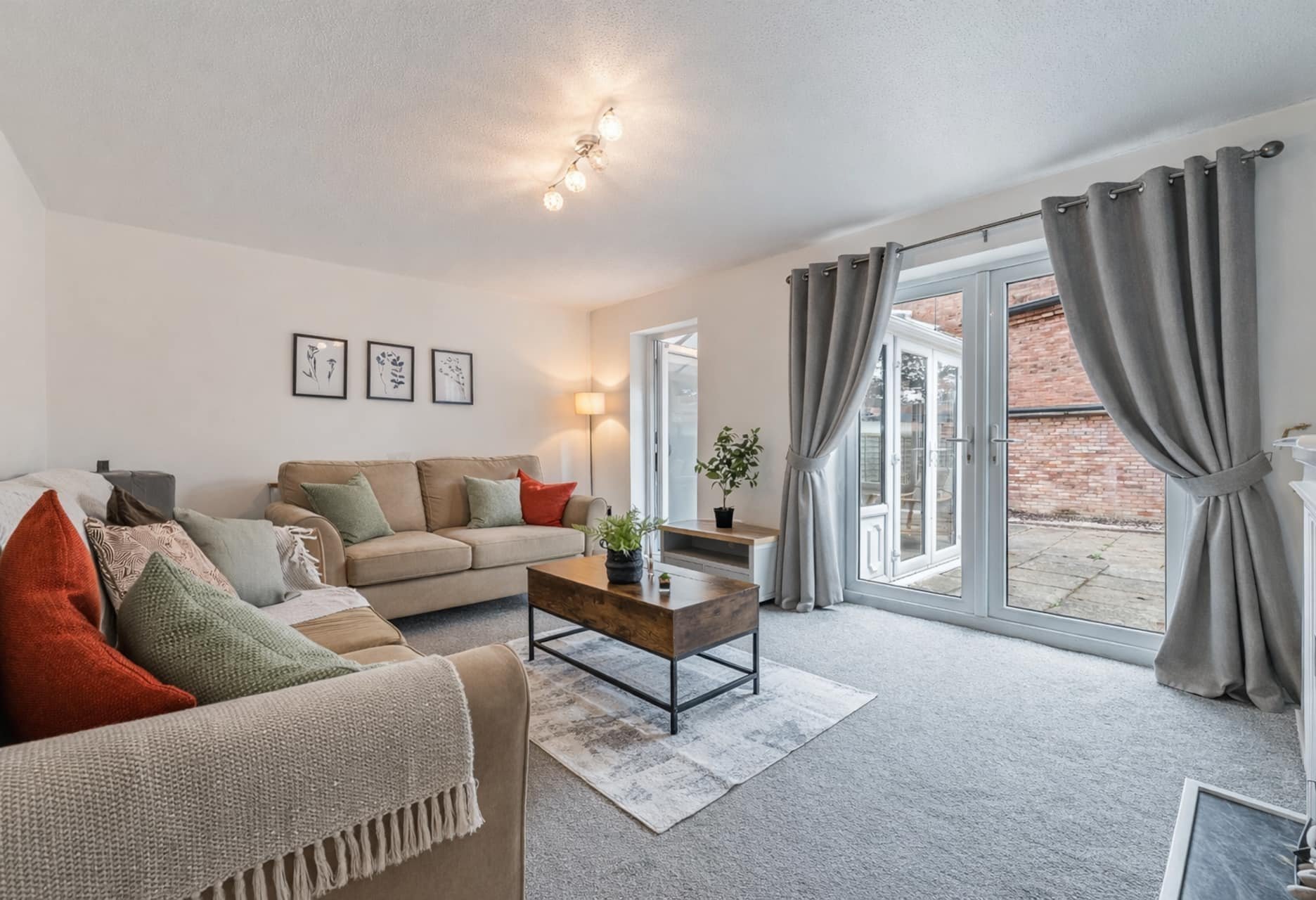 Modern living room with neutral sofas, coffee table, cushions and patio doors to garden