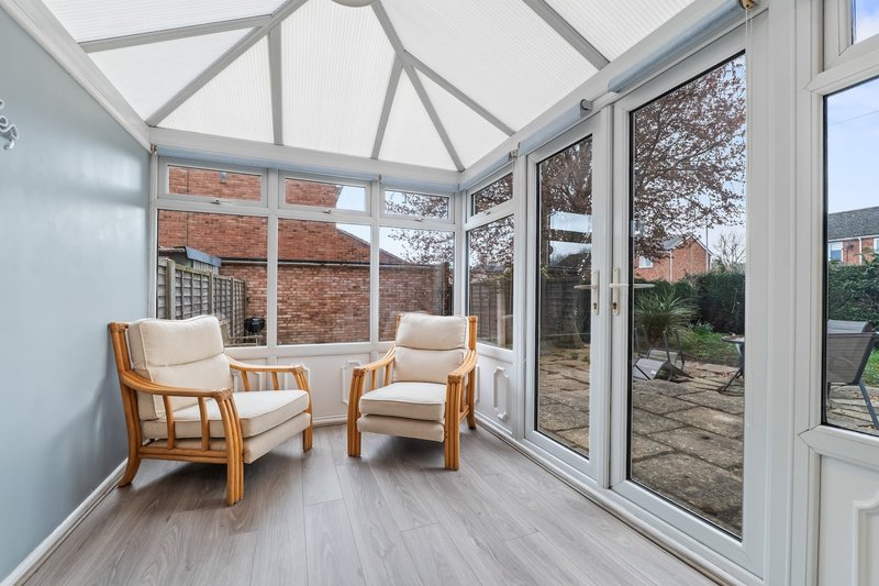 Bright conservatory with two wooden armchairs, polished flooring, and garden views through glazed doors
