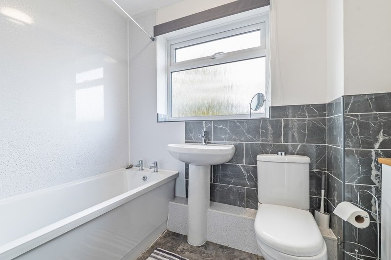 Modern bathroom with bathtub, pedestal sink, toilet, and dark tile wall