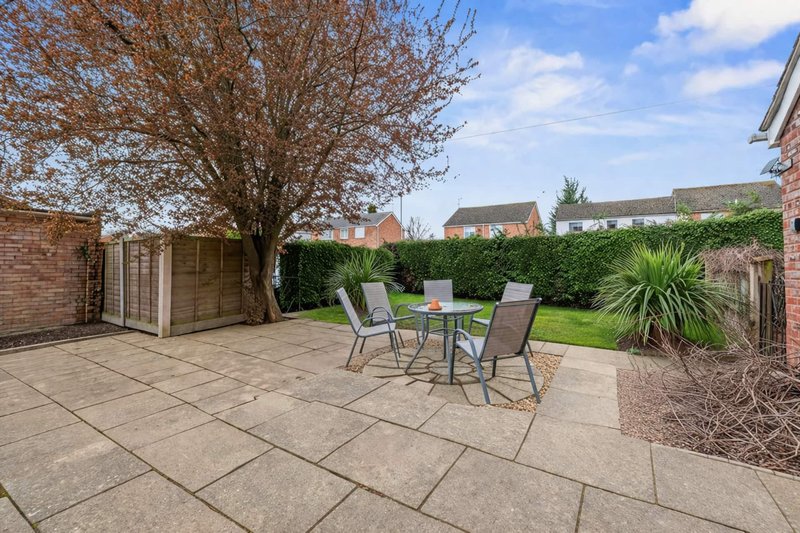 Rear garden patio with paving, garden furniture, hedges and bare tree