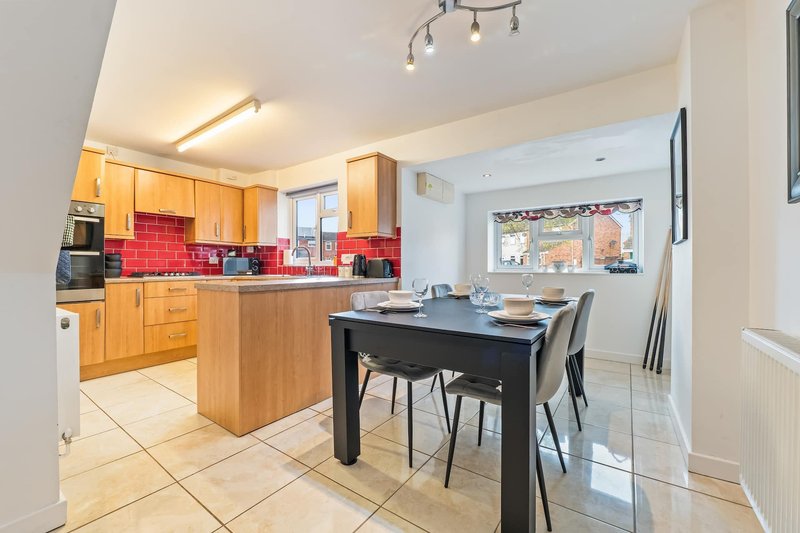 Open-plan kitchen and dining area with wooden cabinetry, red tile backsplash, and black dining table with chairs