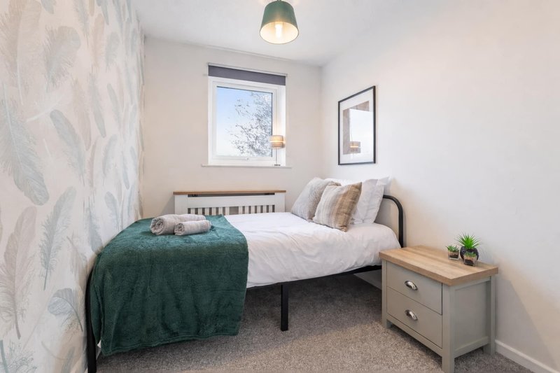 Bedroom with single bed, wooden headboard, green bedding, gray nightstand and window