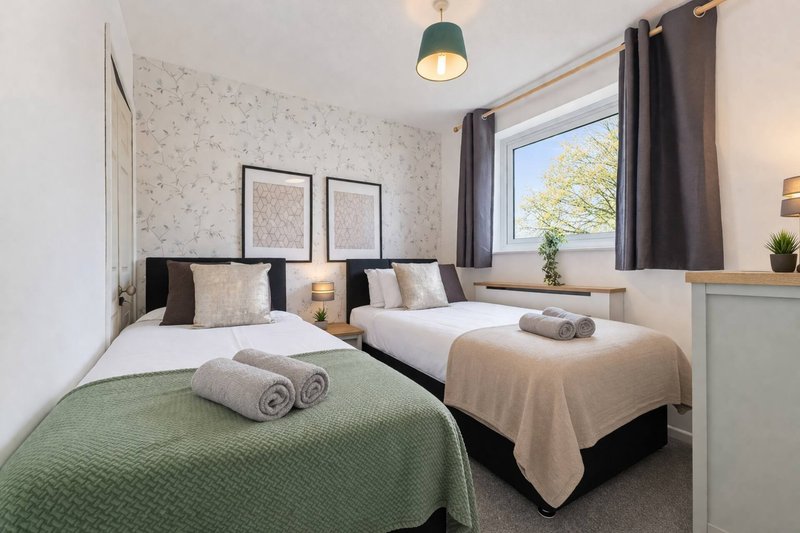 Twin bedroom with green and beige bedding, window view, framed wall art, pendant lighting