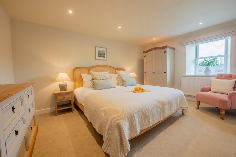 Bright bedroom with double bed, wooden headboard, bedside lamps, white wardrobe and pink armchair