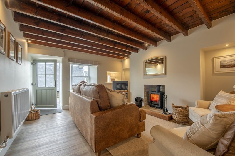 Spacious open-plan living room with exposed wooden beams, leather sofa, electric stove and comfortable seating