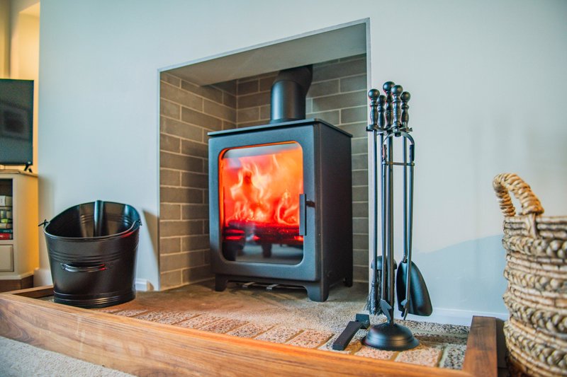 Wood-burning stove with lit fire, fireplace tools, and woven baskets in living room