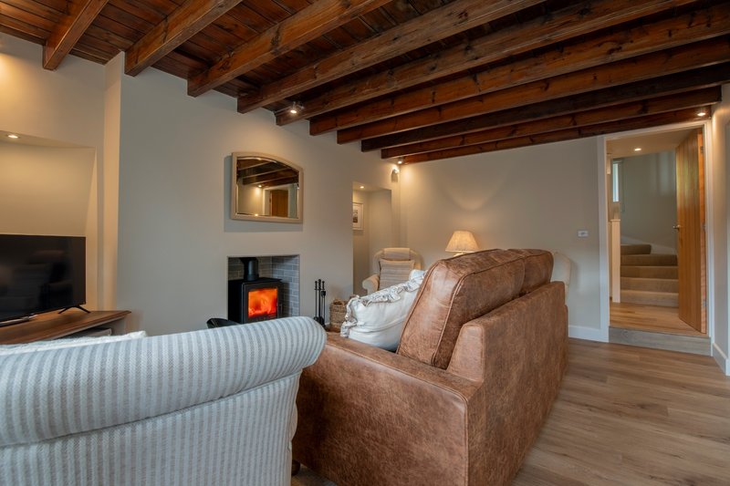 Spacious living room with brown leather sofa, fireplace with glowing insert, exposed wooden beams and wooden flooring