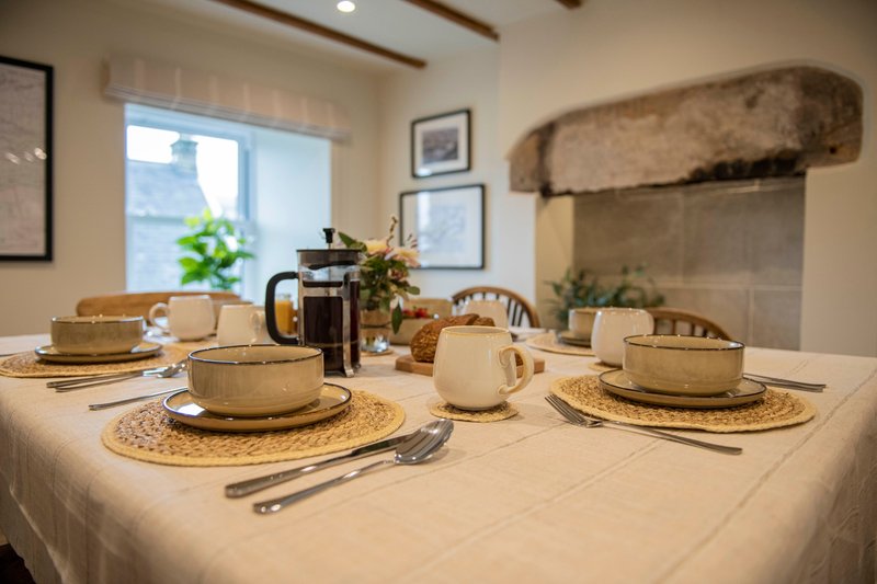 Dining table set for meal service with place settings, teapot, and decorative fireplace backdrop