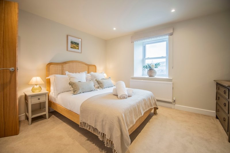 Bright bedroom with wooden bed, white bedding, bedside lamps, and window with radiator