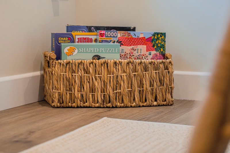 Woven basket storage unit with board games and puzzles on wooden floor