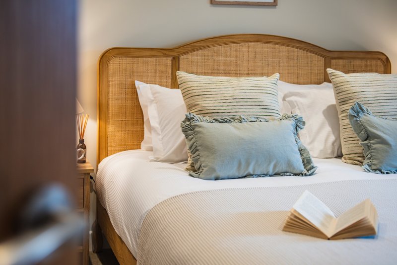 Bedroom with rattan headboard, white bedding, blue and striped pillows, open book