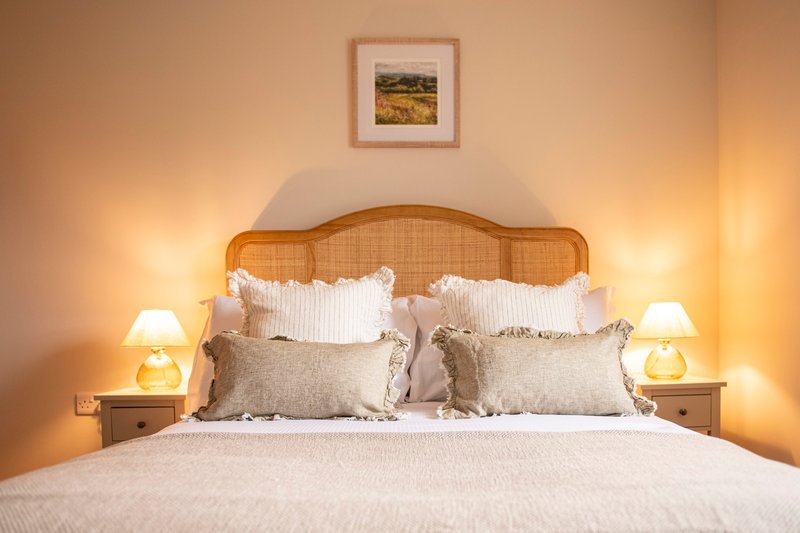 Bedroom with woven headboard, white pillows, beige bedding, and bedside lamps