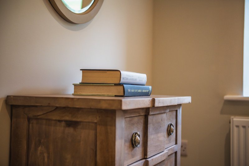 Wooden dresser with stacked books and round mirror on beige wall