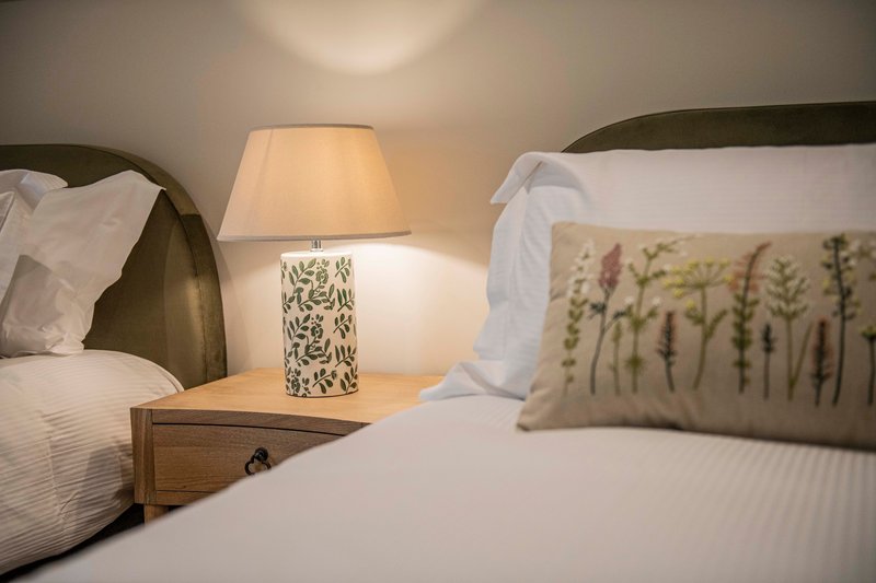 Bedroom with two beds, bedside lamp, cushions and white bedding