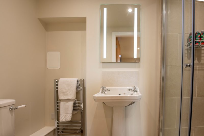 Modern bathroom with pedestal sink, illuminated mirror, heated towel rack and shower enclosure