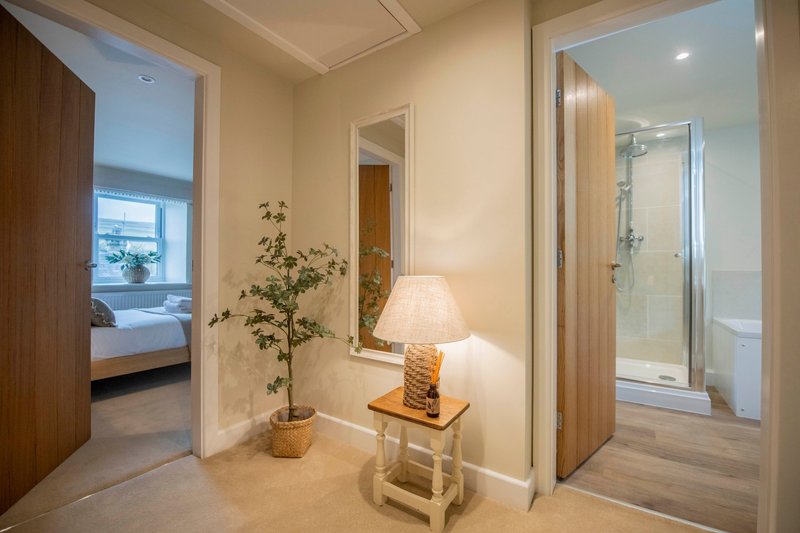 Modern hallway with wooden doors, potted plant, table lamp, and shower enclosure