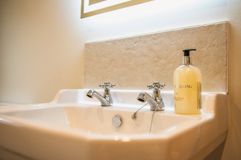 Bathroom sink with dual faucets, soap dispenser, and cream-colored backsplash