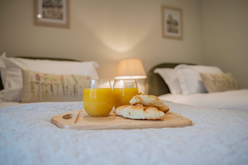 Bedroom with two beds, orange juice and pastries on wooden tray, bedside lamp