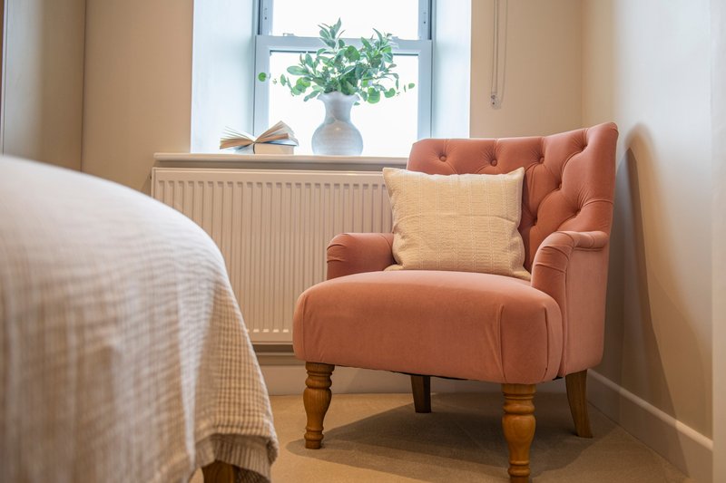 Bedroom with orange armchair, cushions, bed corner, radiator and windowsill with plant