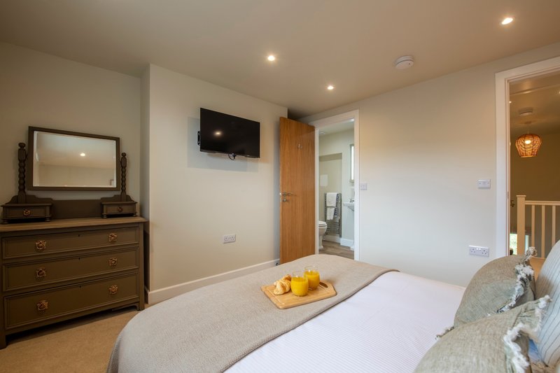 Bedroom with double bed, wooden dresser, wall-mounted TV, and en-suite bathroom visible